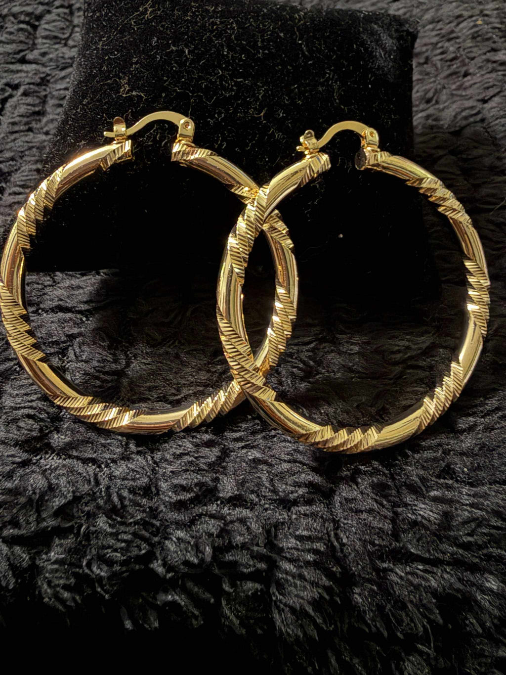 Gold-tone textured hoop earrings with a twisted pattern, shiny finish, a classic round shape, representing Bambi's style.